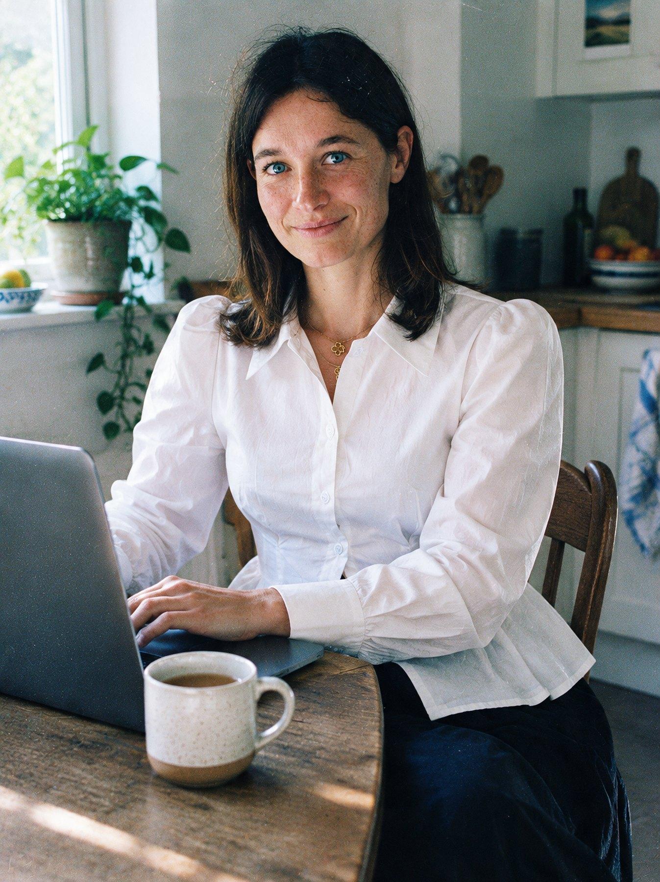 The Collar Shirt in White, seated at a laptop with a coffee mug, front view