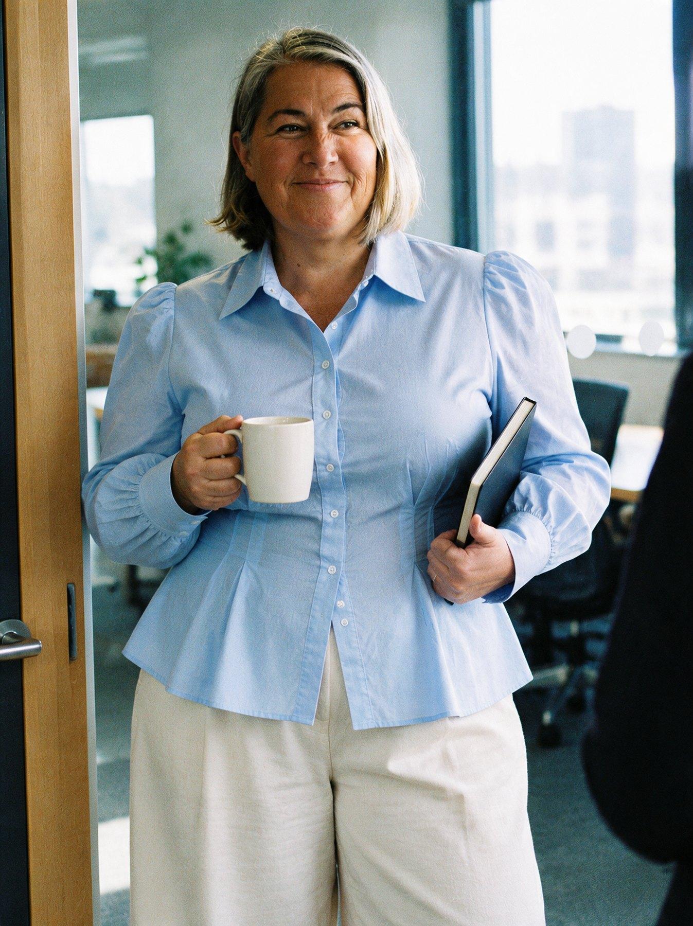 The Collar Shirt in Sky Blue, standing in an office doorway holding a mug, front view