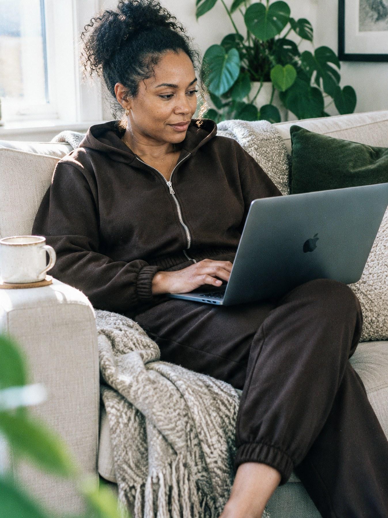 The Lounge Set in Brown, styled at home, seated on the sofa with a laptop