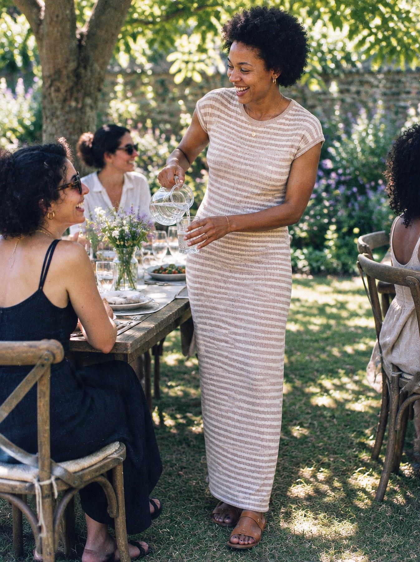 The Stripe Maxi in Beige, full length, pouring water at an outdoor lunch