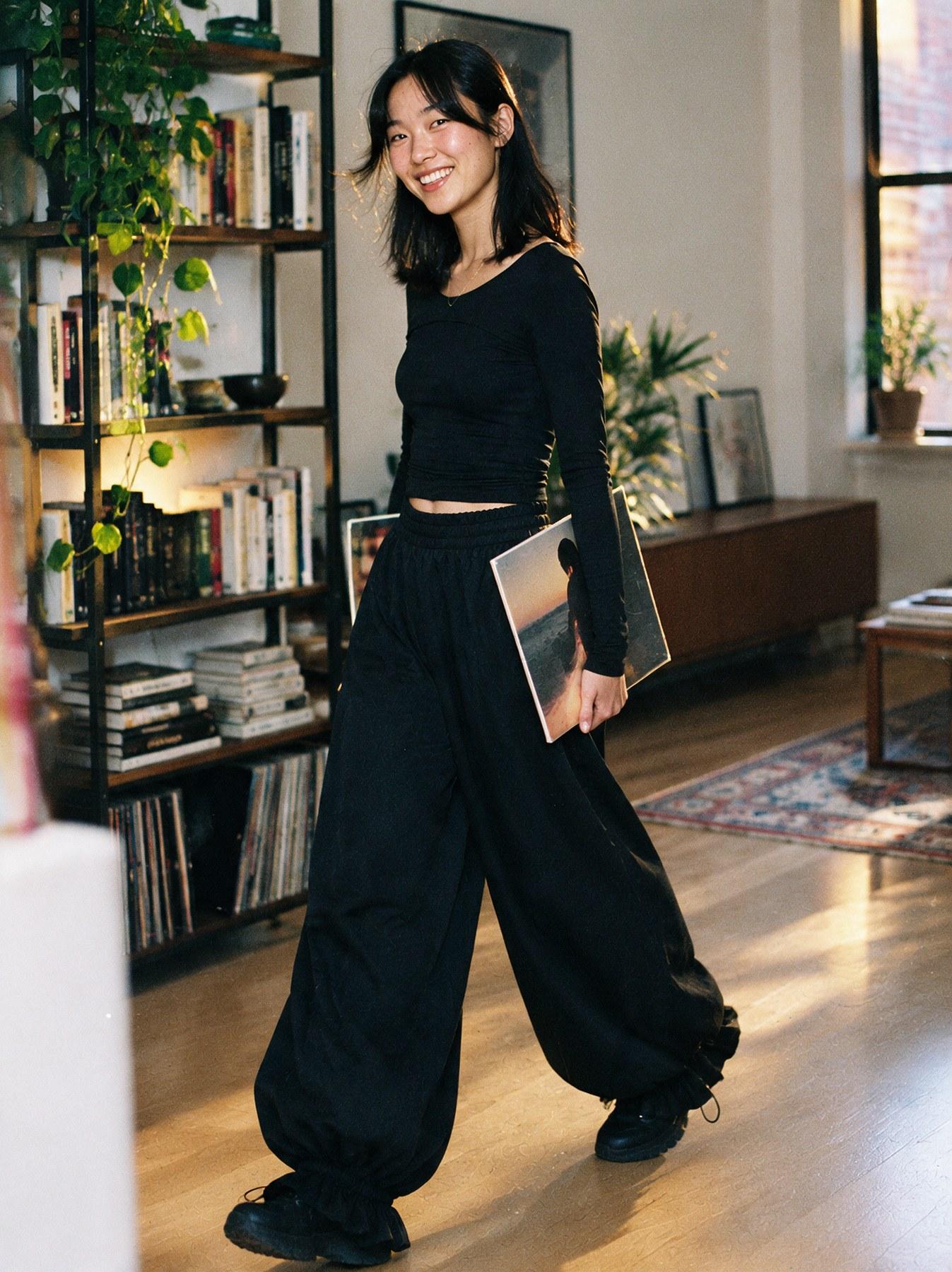 The Parachute Trouser in Black, three-quarter view, walking indoors holding a record