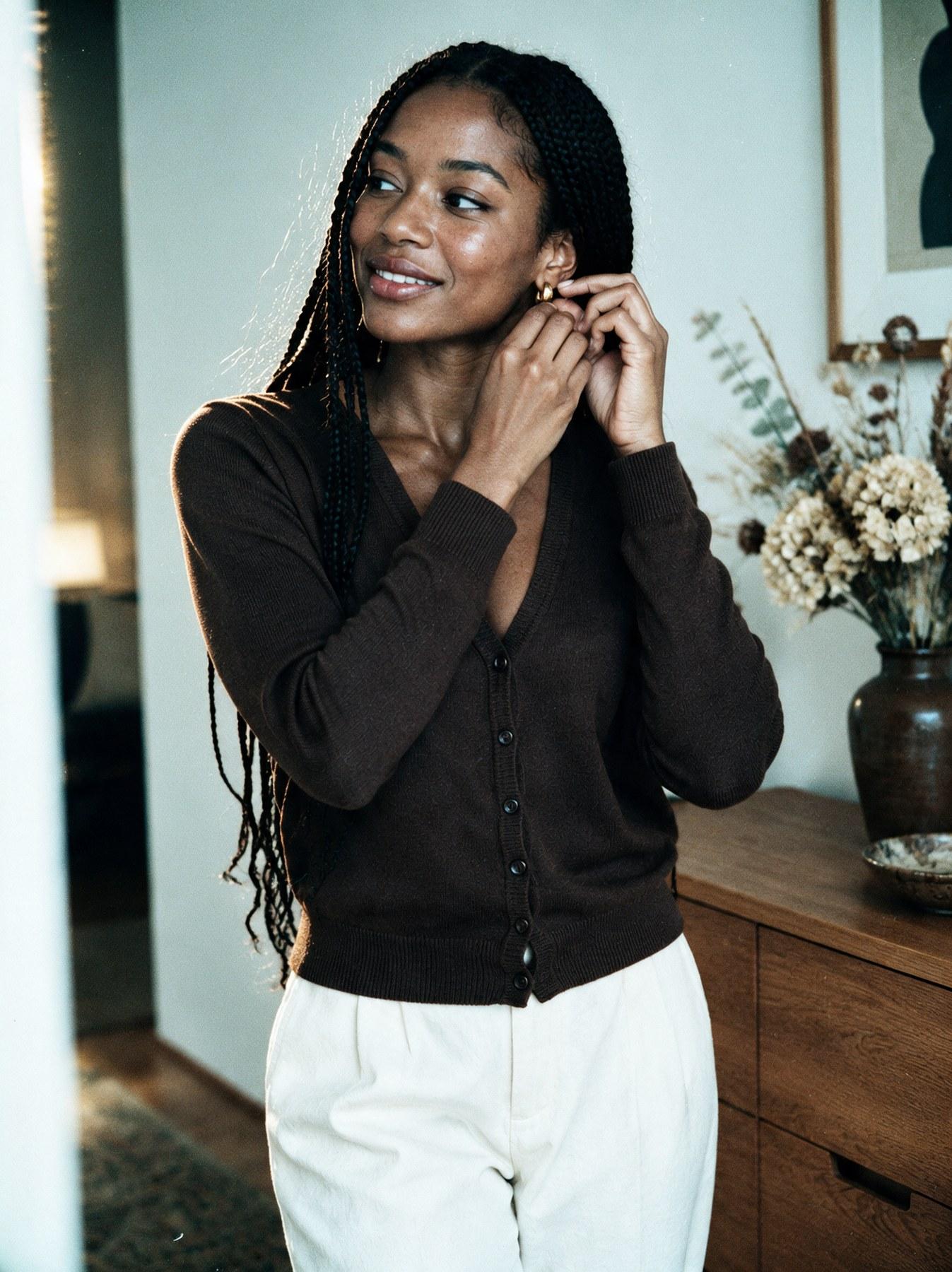 The Fine-Knit Cardigan in Brown, three-quarter view, adjusting an earring