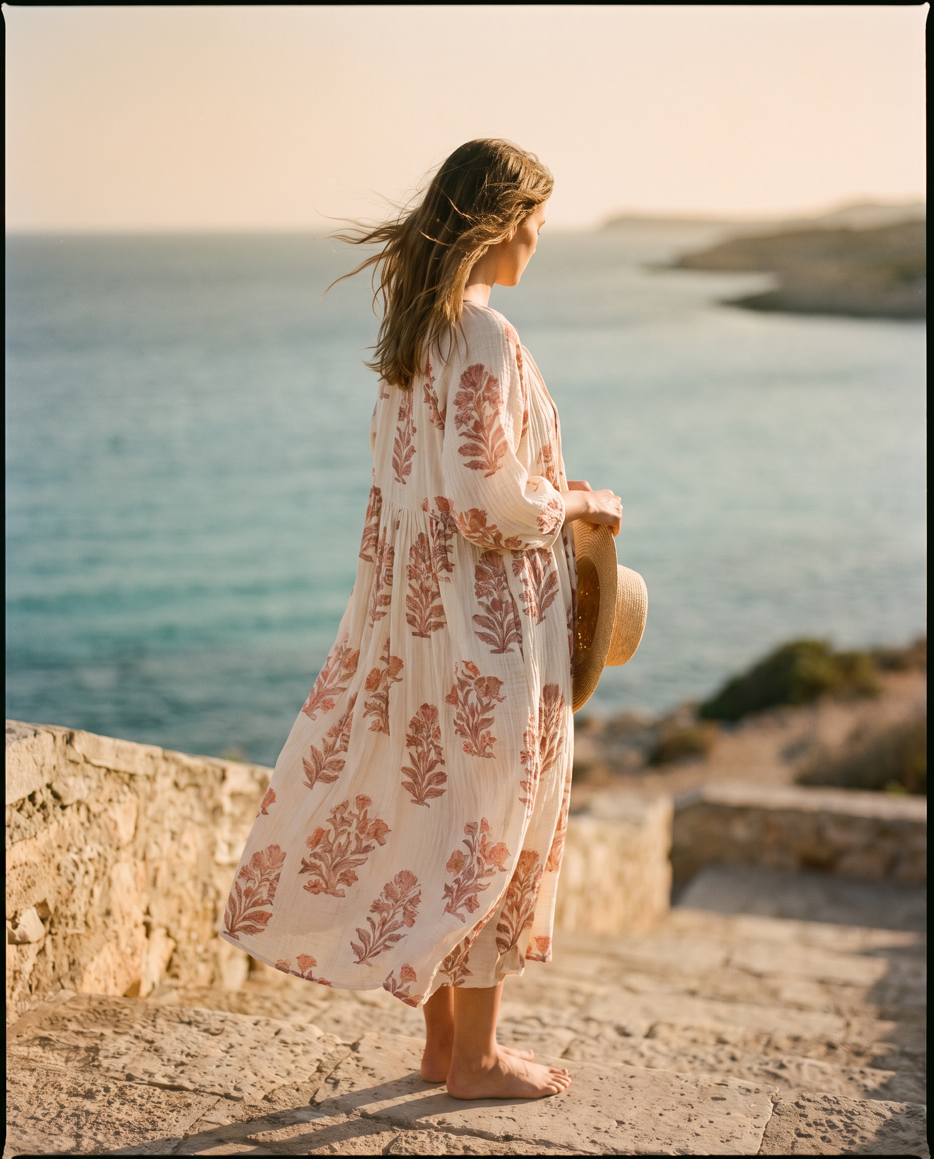 Woman in a printed organic cotton muslin dress on sun-bleached coastal steps
