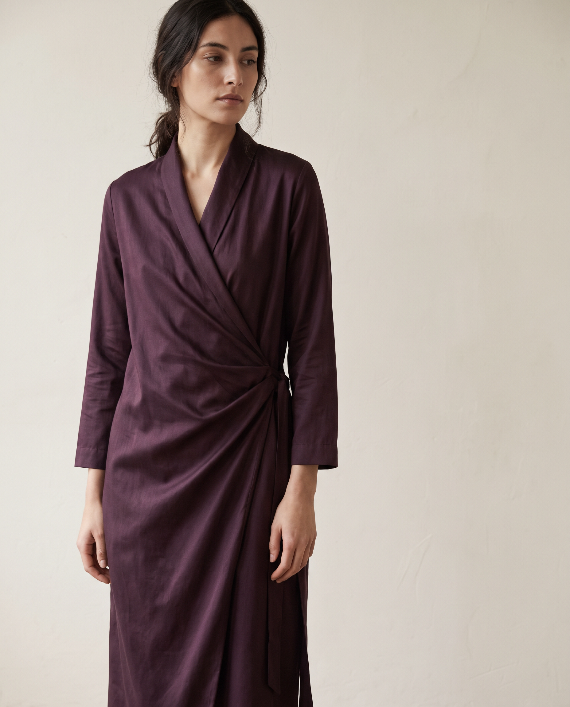Aubergine cotton sateen wrap dress against a cream wall
